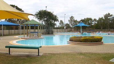 Wide shot of Bethania Aquatic Centre outdoor pool with a white umbrella to the left and smaller blue umbrella covering the pool