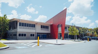 Outside the Logan Metro Sports and Events centre. Grey and white building with large red pointing feature in the centre of the building.
